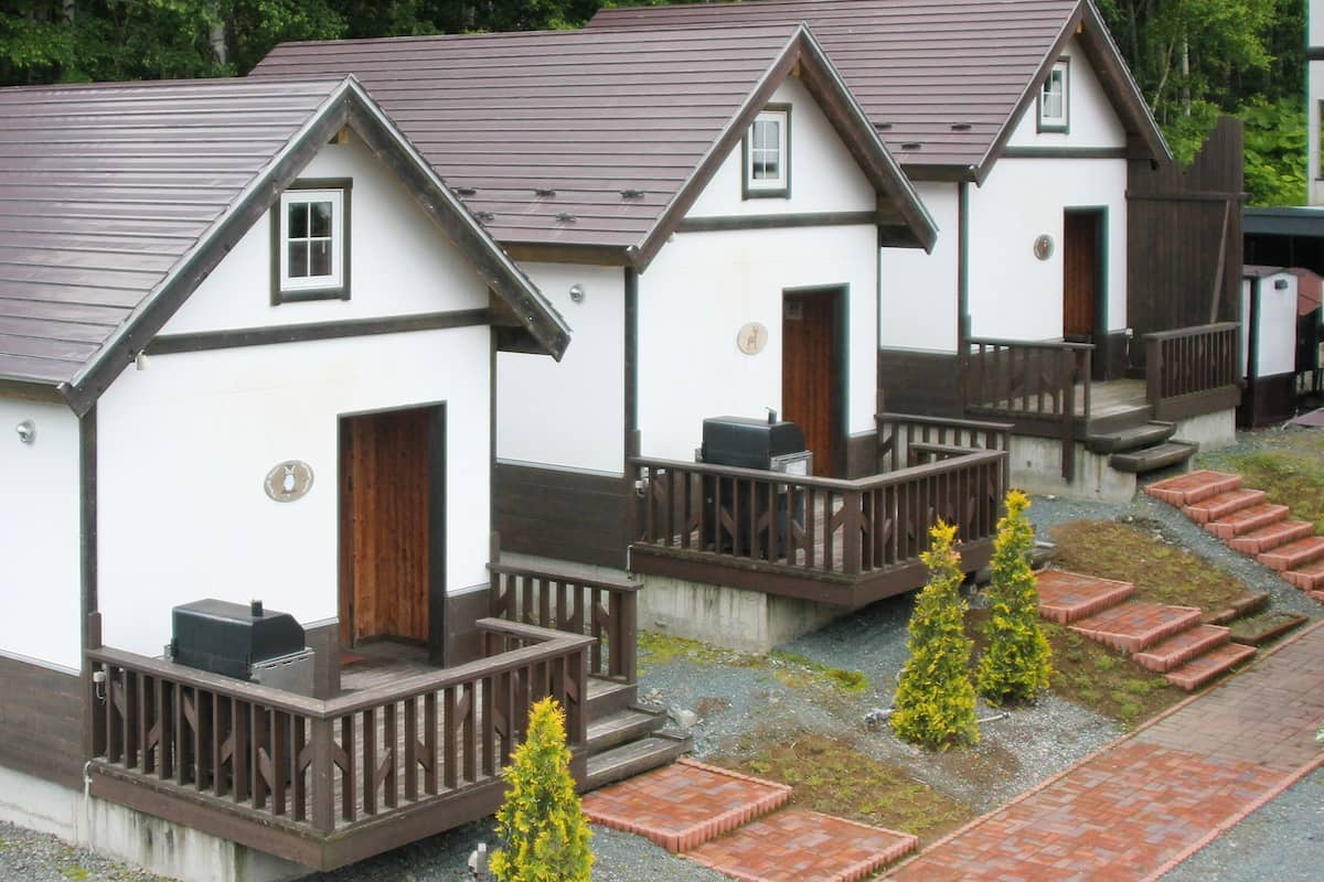 Eine Reihe kleiner, weißer Holzhütten mit braunen Dächern und Holzbalkonen, jeweils mit einer Tür und einem Fenster.
