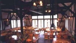A spacious indoor area with high ceilings and exposed wooden beams. There are multiple tables and chairs arranged in a casual layout, suggesting a dining or meeting area. - Petit Hotel Gracey Tomamu (Shimukappu)