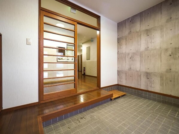 A room with a sliding door leading to a hallway, a concrete wall, and a tiled floor.