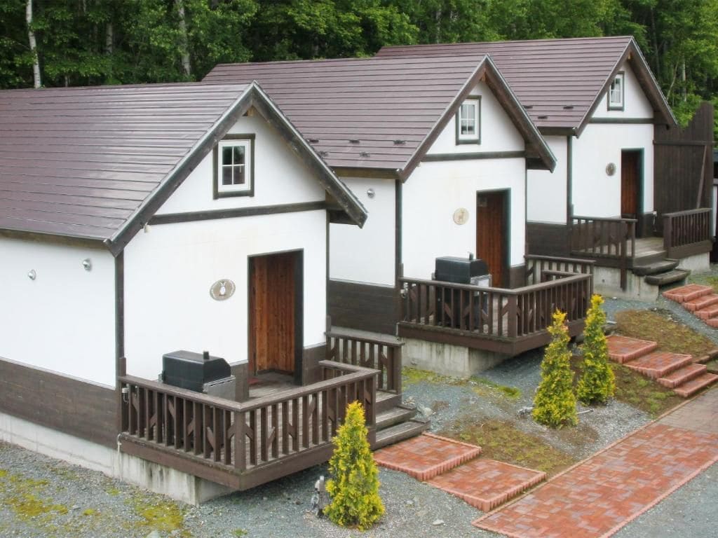 Una hilera de cabañas pequeñas, de color blanco con techos marrones y barandillas de madera, cada una con una puerta y una ventana.