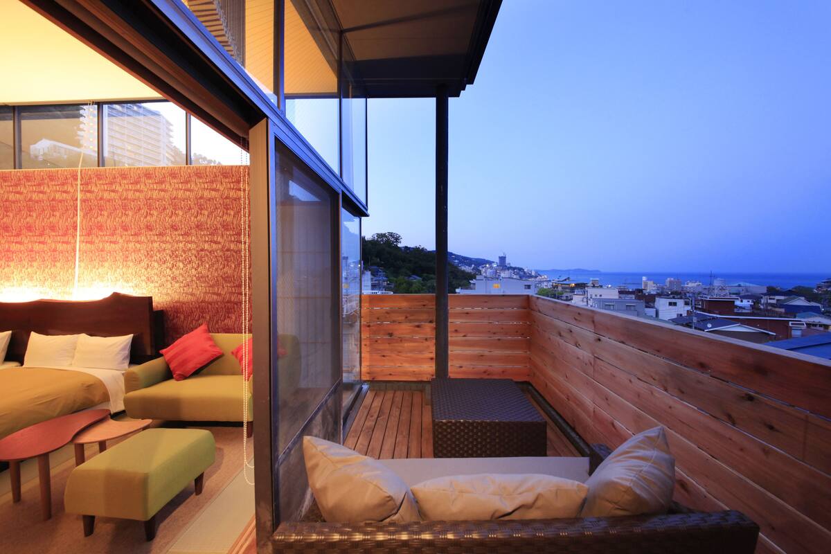 Un balcón con piso de madera, una zona de estar con cojines y vista panorámica de la ciudad.
