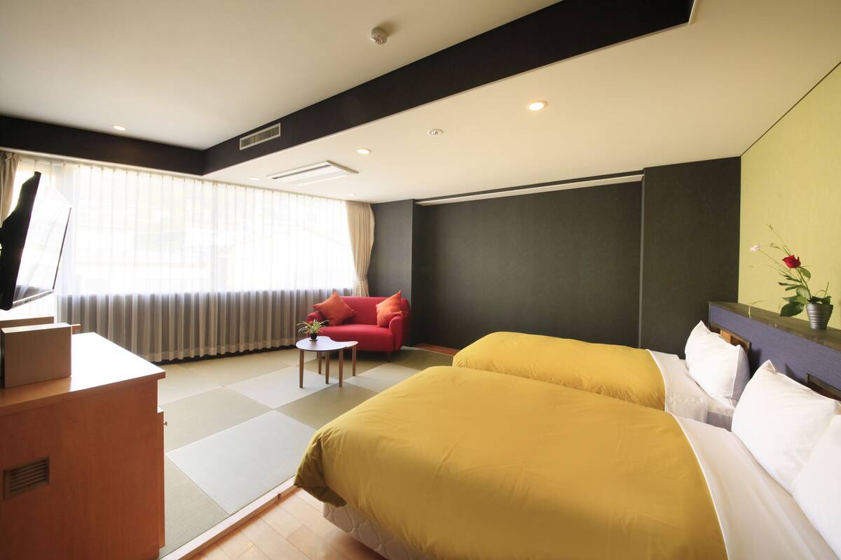 Habitación de hotel con dos camas, un sofá rojo, una mesita y un televisor sobre un escritorio.