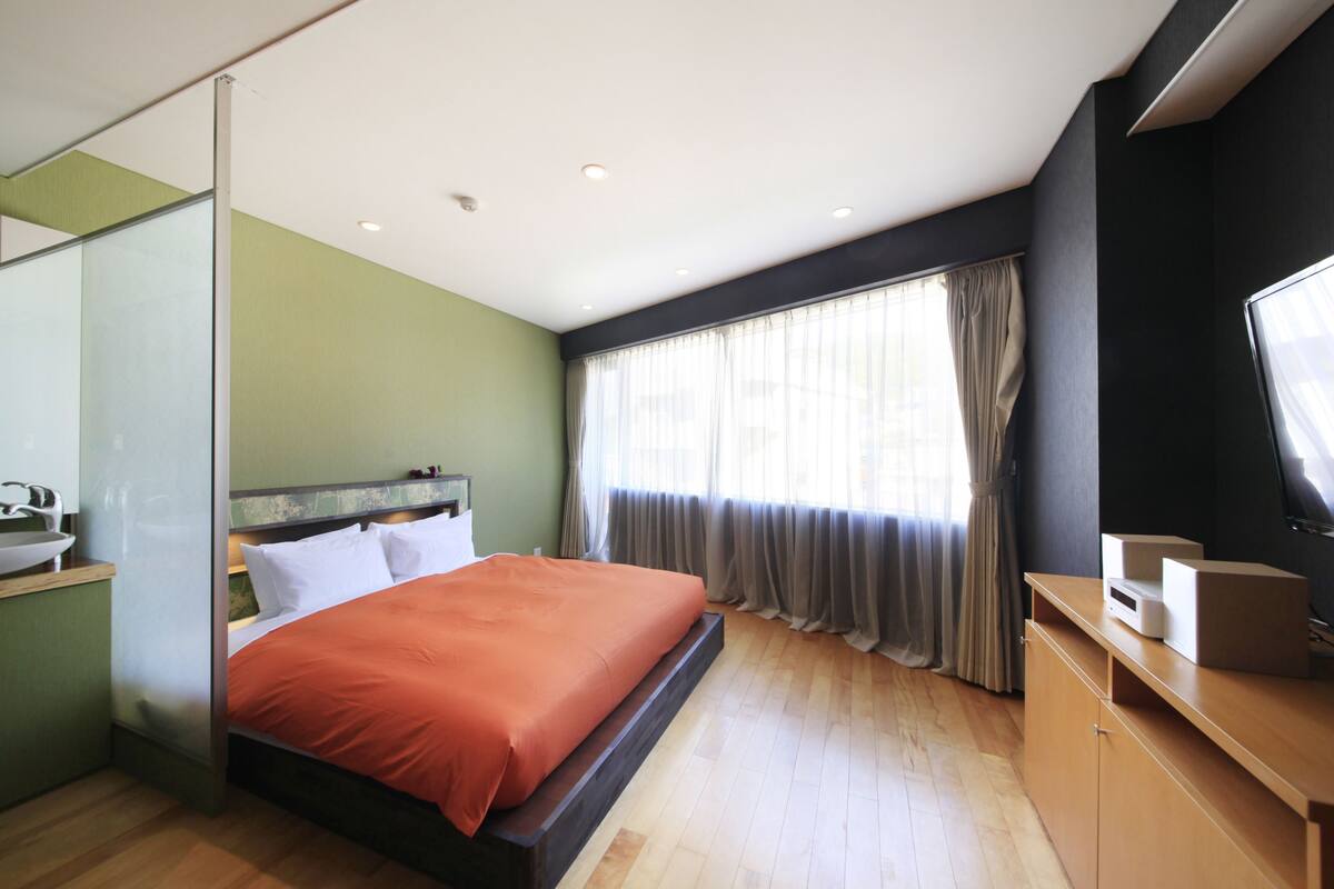 Una habitación de hotel moderna con cama, escritorio, televisión y ventana con cortinas.