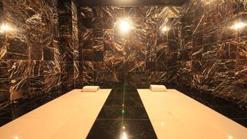Un cuarto de spa con paredes de mármol negro, un suelo negro reflectante en el centro y dos toallas blancas sobre bancos blancos.