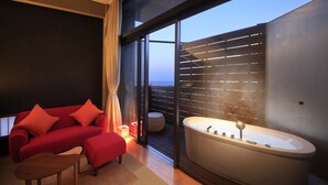 A modern bathroom with a large bathtub, a red sofa, and a view of the sky through a large window. - Atami Tensui (Atami)