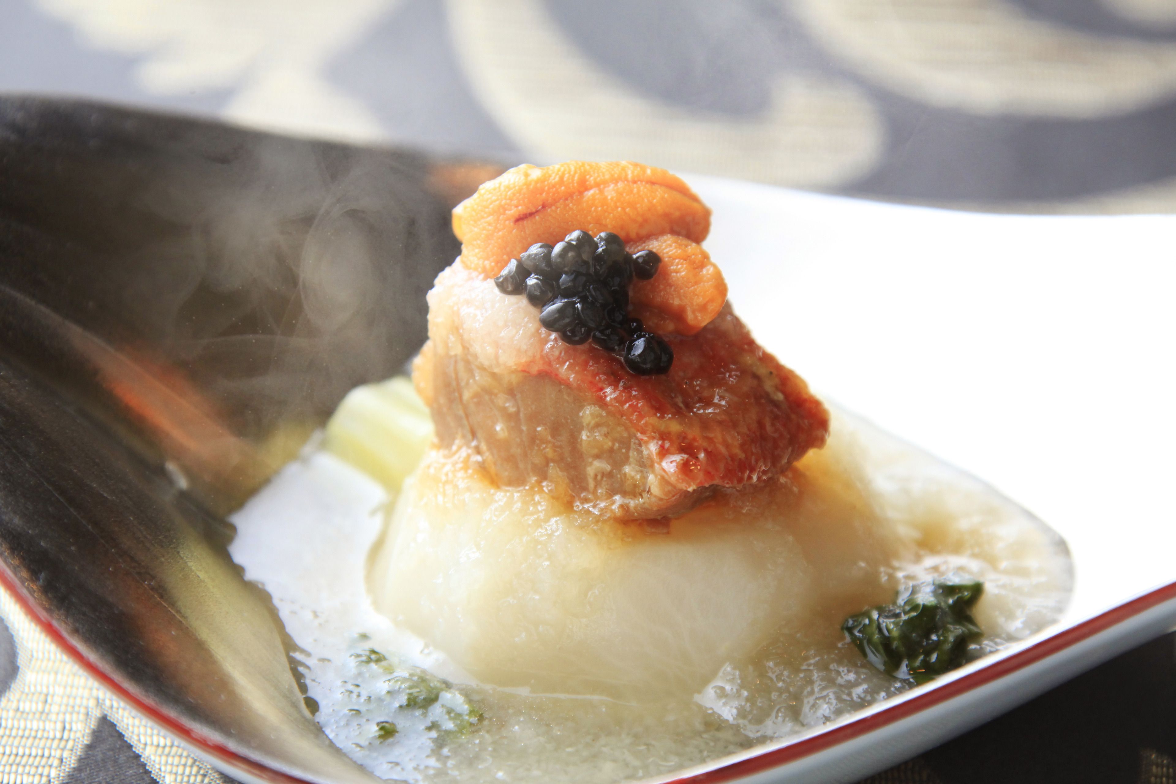 Un plato con caldo transparente y un trozo de carne, adornado con elementos negros y anaranjados.