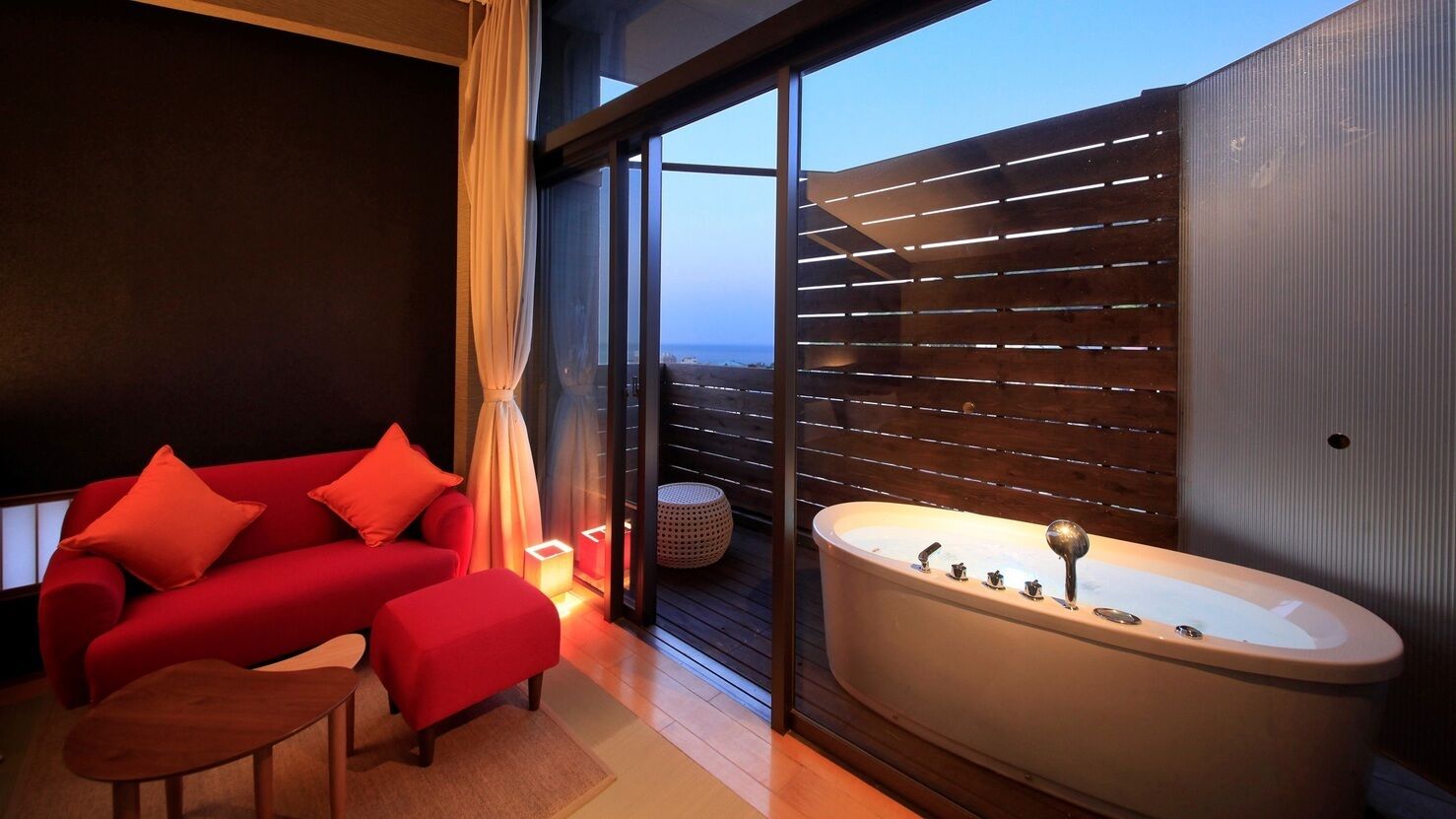 Une chambre moderne avec un canapé rouge, une petite table en bois et une grande baignoire.