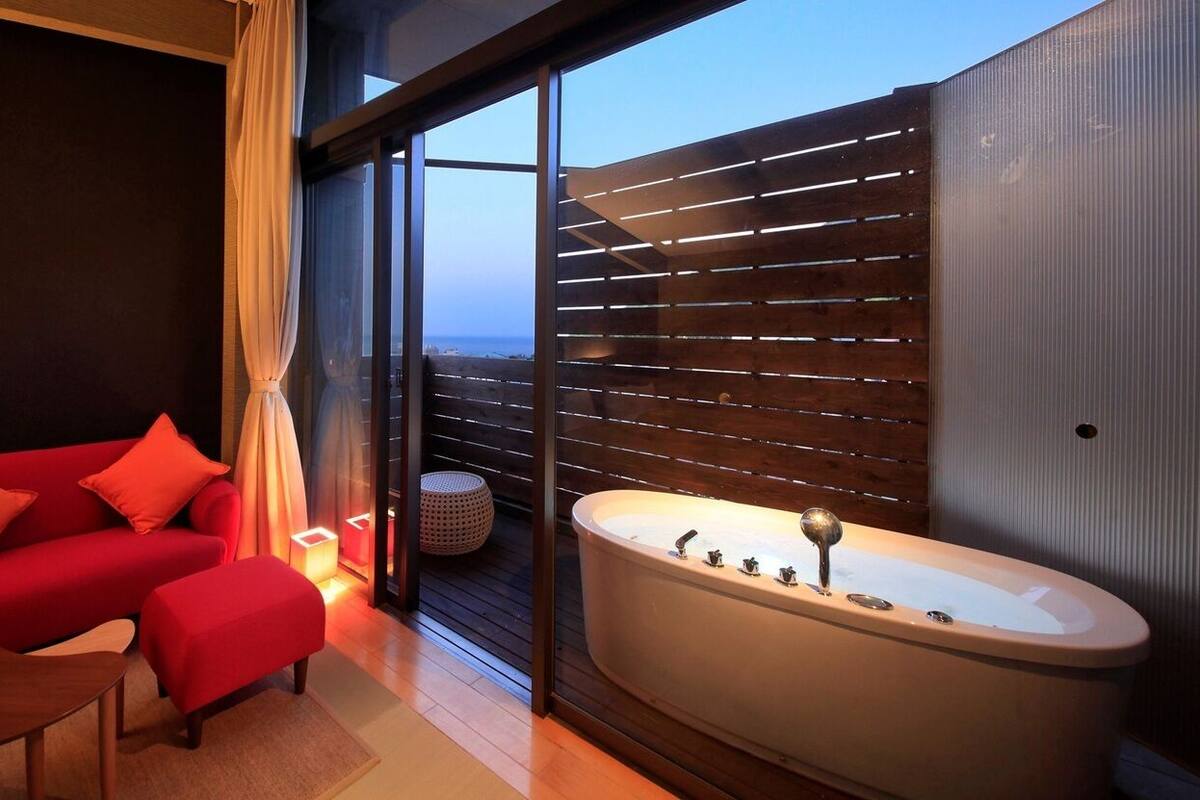Una habitación moderna con un sofá rojo, una pequeña mesa de madera y una bañera grande.