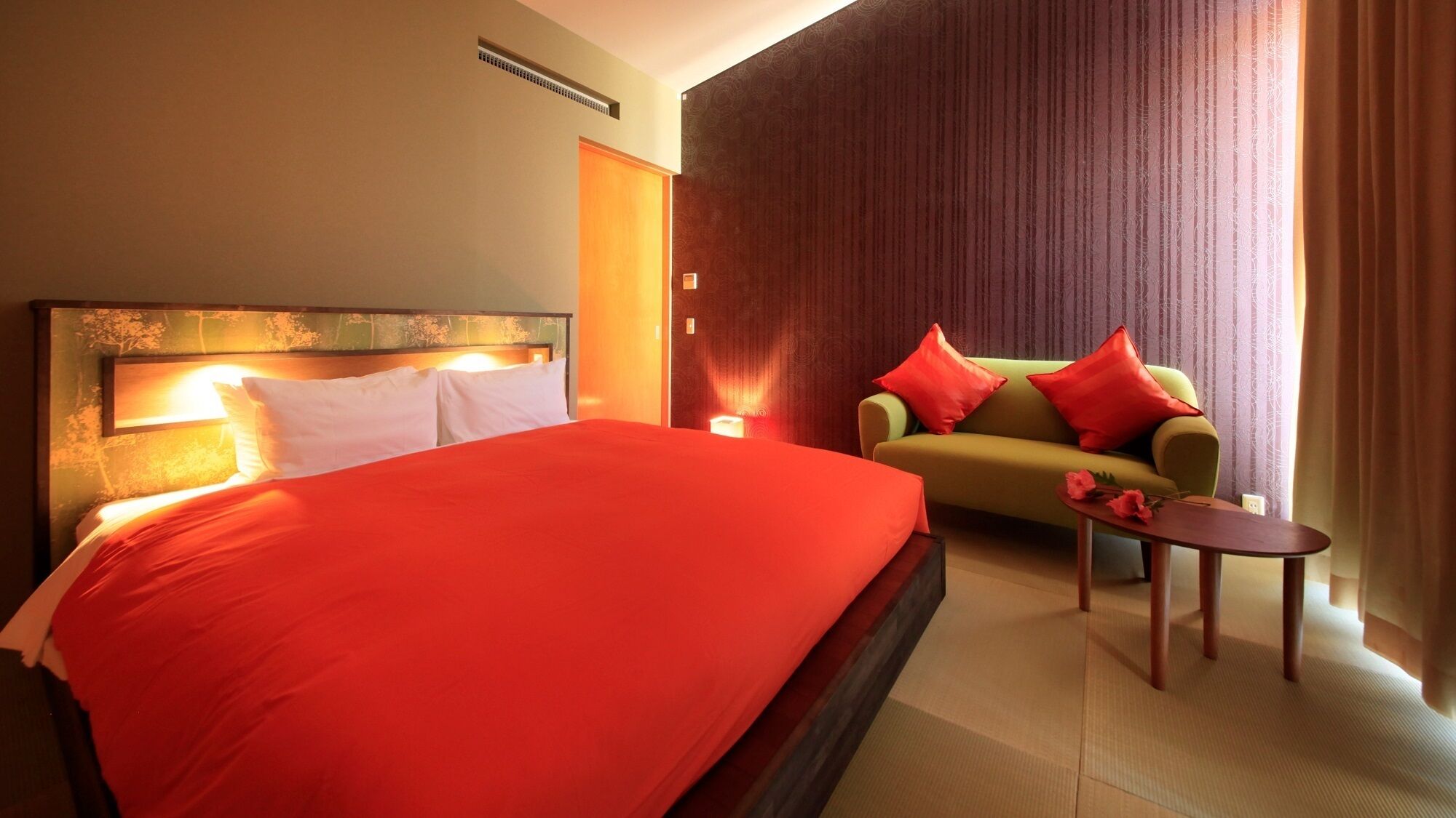 A hotel room with a large bed, a sofa, a small table, and a wall-mounted heater.