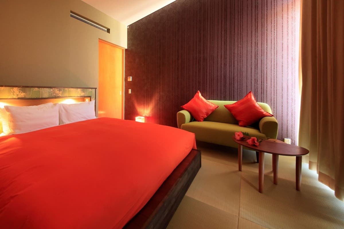 A hotel room with a large bed, a sofa, a small table, and a wall-mounted heater.