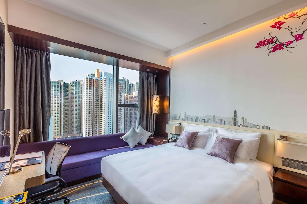 A hotel room with a large bed, a desk, and a view of tall buildings.