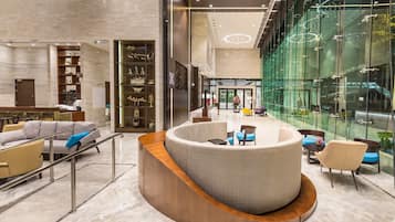 Um lobby moderno com balcão de recepção curvo, área de estar e paredes de vidro que oferecem vista para o exterior.
