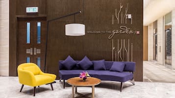 Un hall con un sofá púrpura, un sillón amarillo y una mesa de centro redonda de madera con un centro de flores.