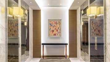 Un moderno vestíbulo de hotel con pisos de mármol, una mesa consola central y un colorido cuadro abstracto en la pared.