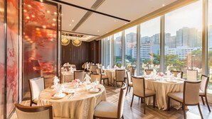 A restaurant with round tables, chairs, and a city view through large windows.