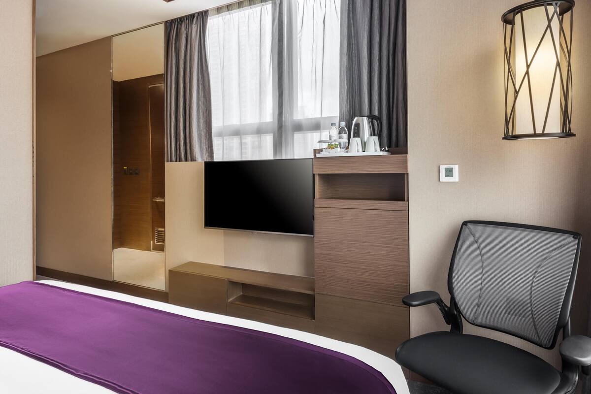 A hotel room with a bed, a TV, a desk with a chair, and a shower area.