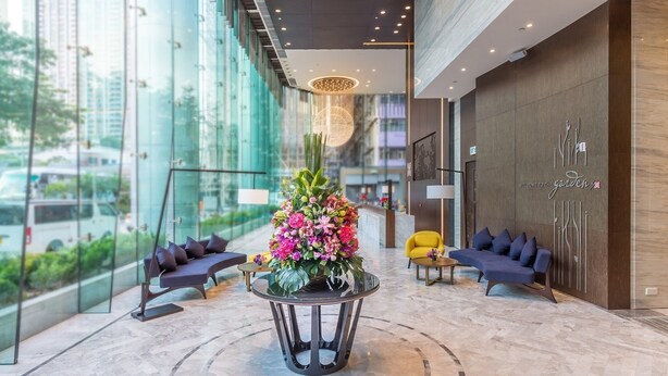 A modern lobby with a large glass wall, a central floral arrangement, and seating areas.