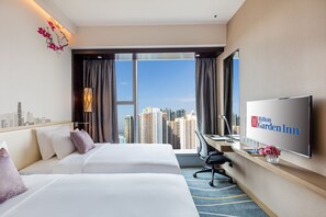 A hotel room with two beds, a desk, a TV, and a view of the city skyline. - Hilton Garden Inn Hong Kong Mongkok (Kowloon)