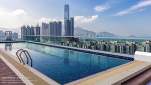 A rooftop swimming pool with a cityscape view, including high-rise buildings and a distant mountain range.