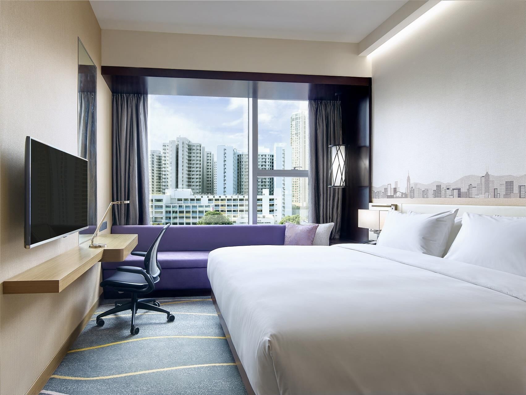 Een hotelkamer met een bed, bureau, stoel, televisie en uitzicht op de stad.