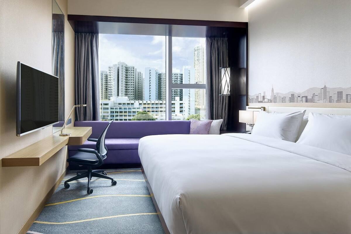 A hotel room with a bed, a desk, a chair, a TV, and a city view.