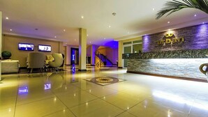 A hotel lobby with a reception desk, seating area, and a staircase.