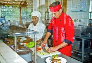 Un chef prepara alimentos en una cocina con mostradores de acero inoxidable y una división de vidrio.