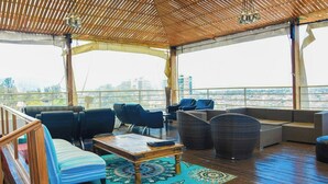 A covered outdoor seating area with a wooden deck, cushioned seating, and a view of the cityscape.