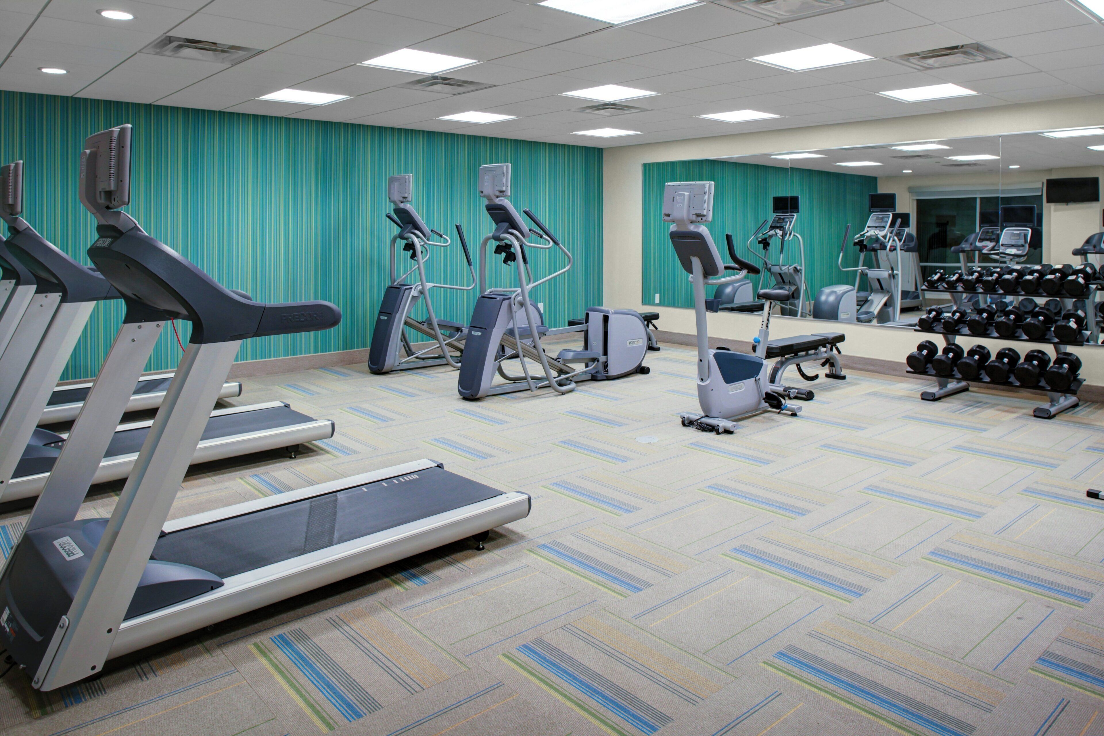 A gym with treadmills, elliptical machines, and dumbbells.