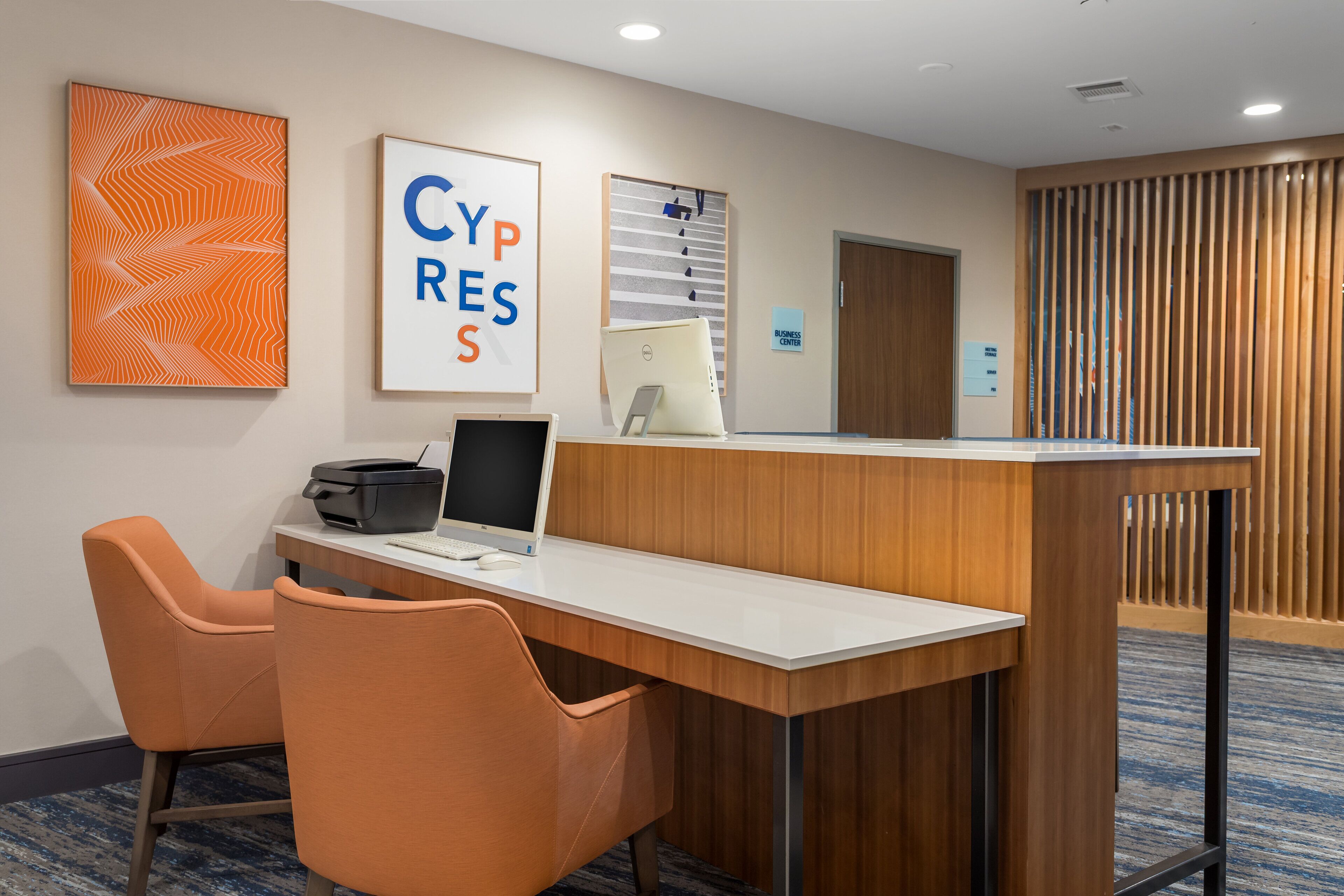 A hotel reception area with a desk, two orange chairs, a computer, and a sign that reads "CYPRESS."