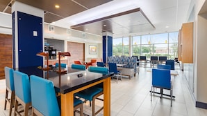 A modern dining area with a black bar, blue chairs, and a brick accent wall. - Holiday Inn Express & Suites Houston NW - Cypress Grand Pky by IHG (Cypress)