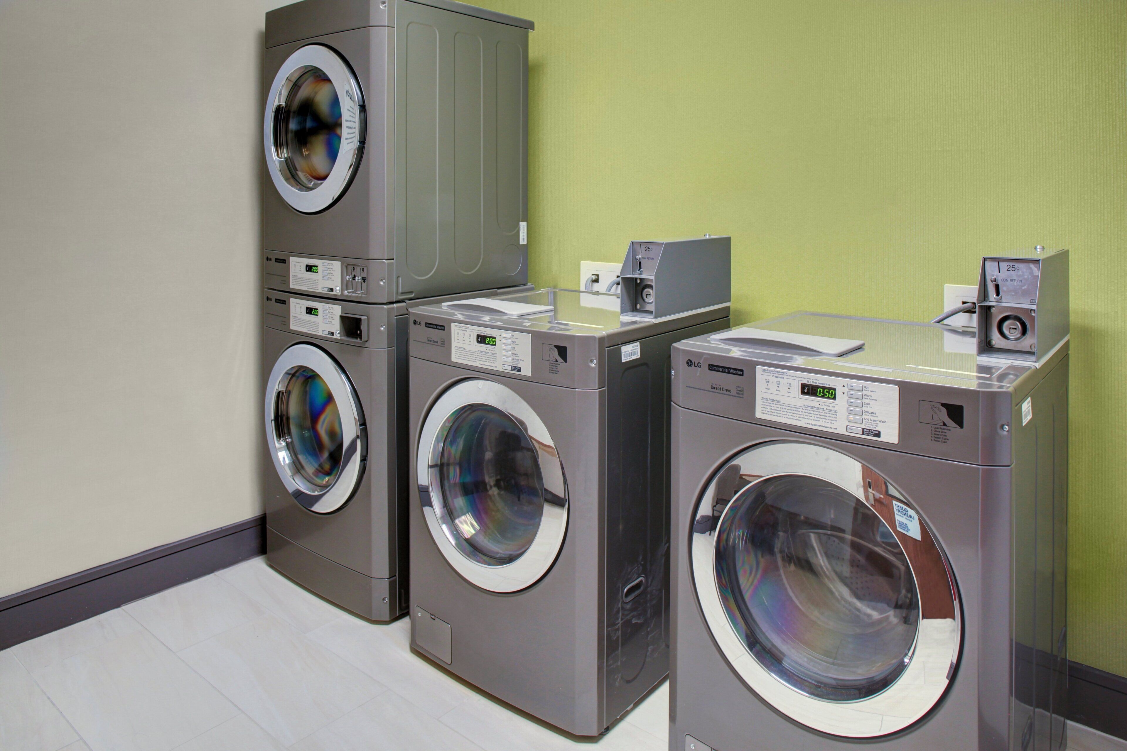 A laundry facility with multiple washing machines and dryers, a control panel, and a coin return slot.