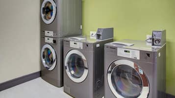 A laundry facility with multiple washing machines and dryers, a control panel, and a coin return slot.
