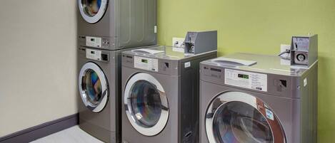 A laundry facility with multiple washing machines and dryers, a control panel, and a coin return slot.