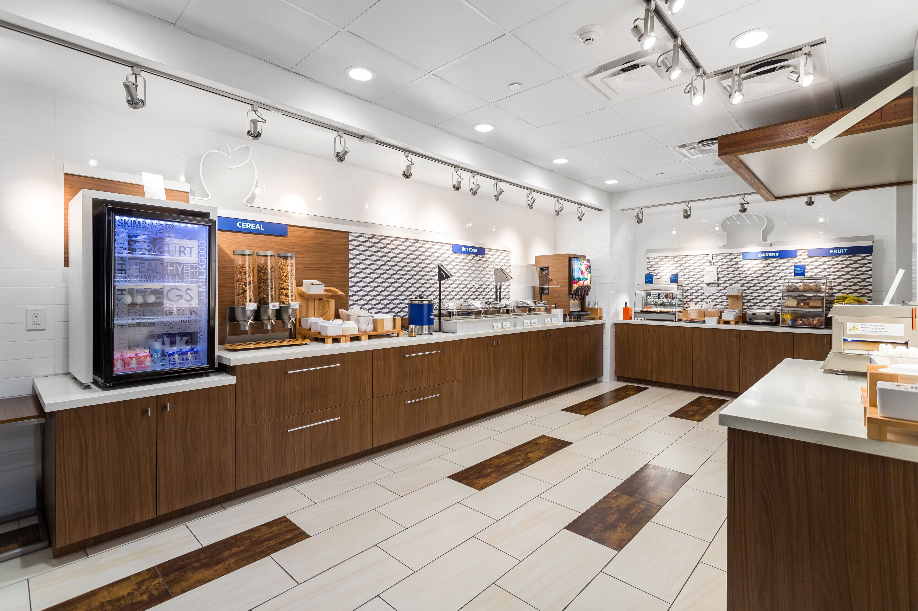 Un espace cuisine moderne doté d’un réfrigérateur-vitrine, de meubles en bois et d’un comptoir où sont exposés divers produits alimentaires.