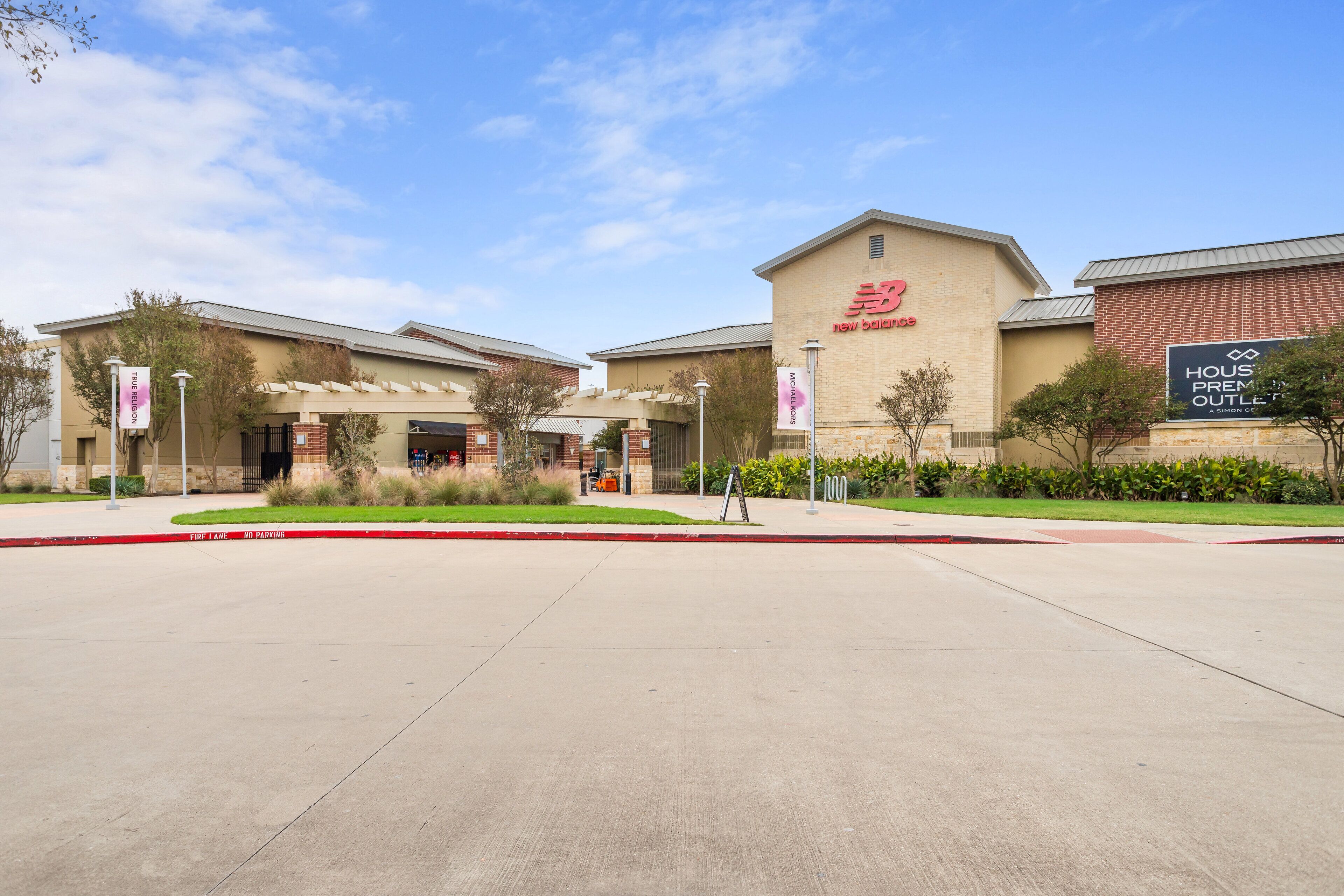 A commercial building with a prominent 'New Balance' sign, a 'House Premium Outlet' sign, and a clear sky.