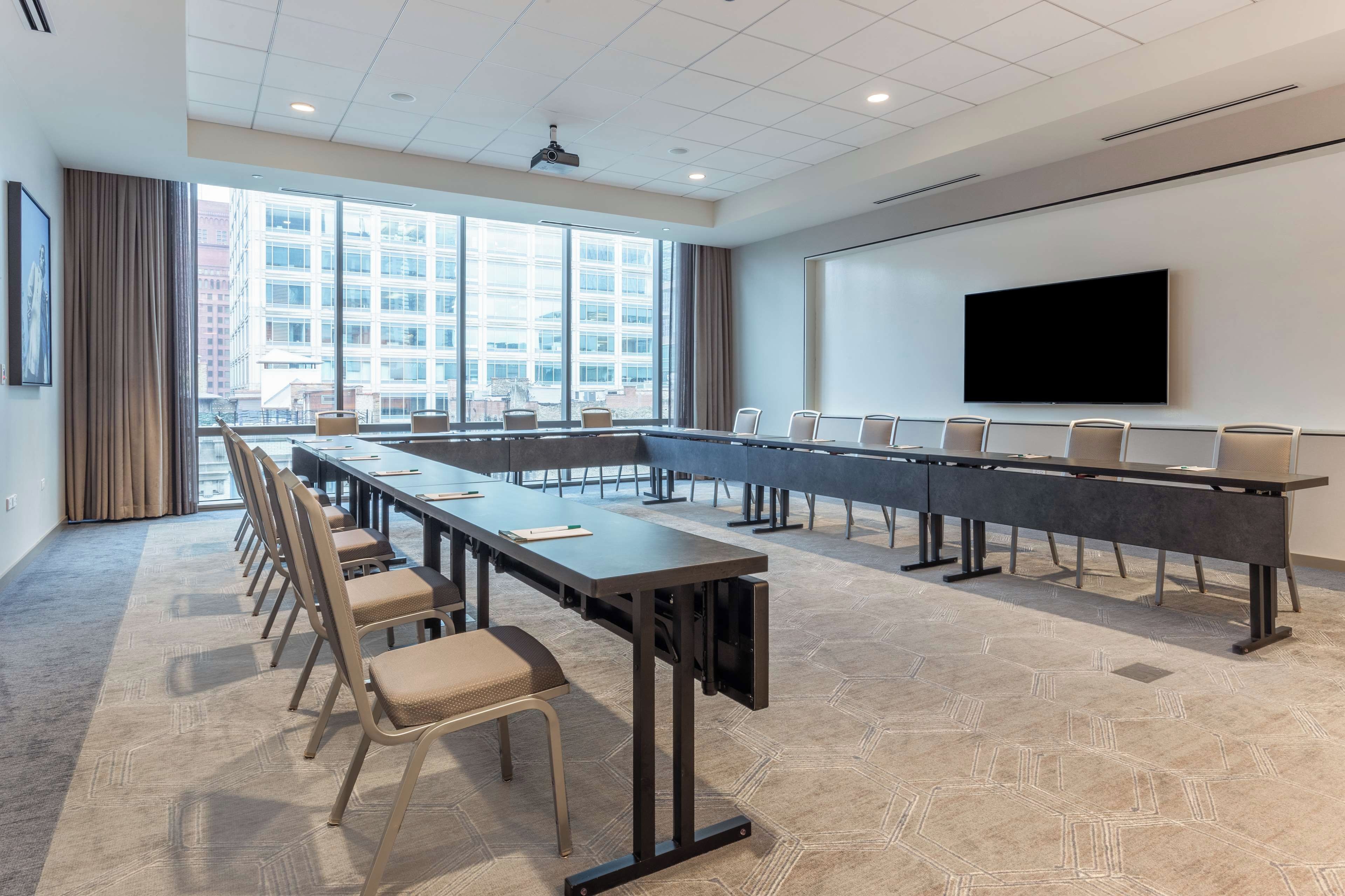 A conference room with a long table, chairs, a projector, and a large screen.