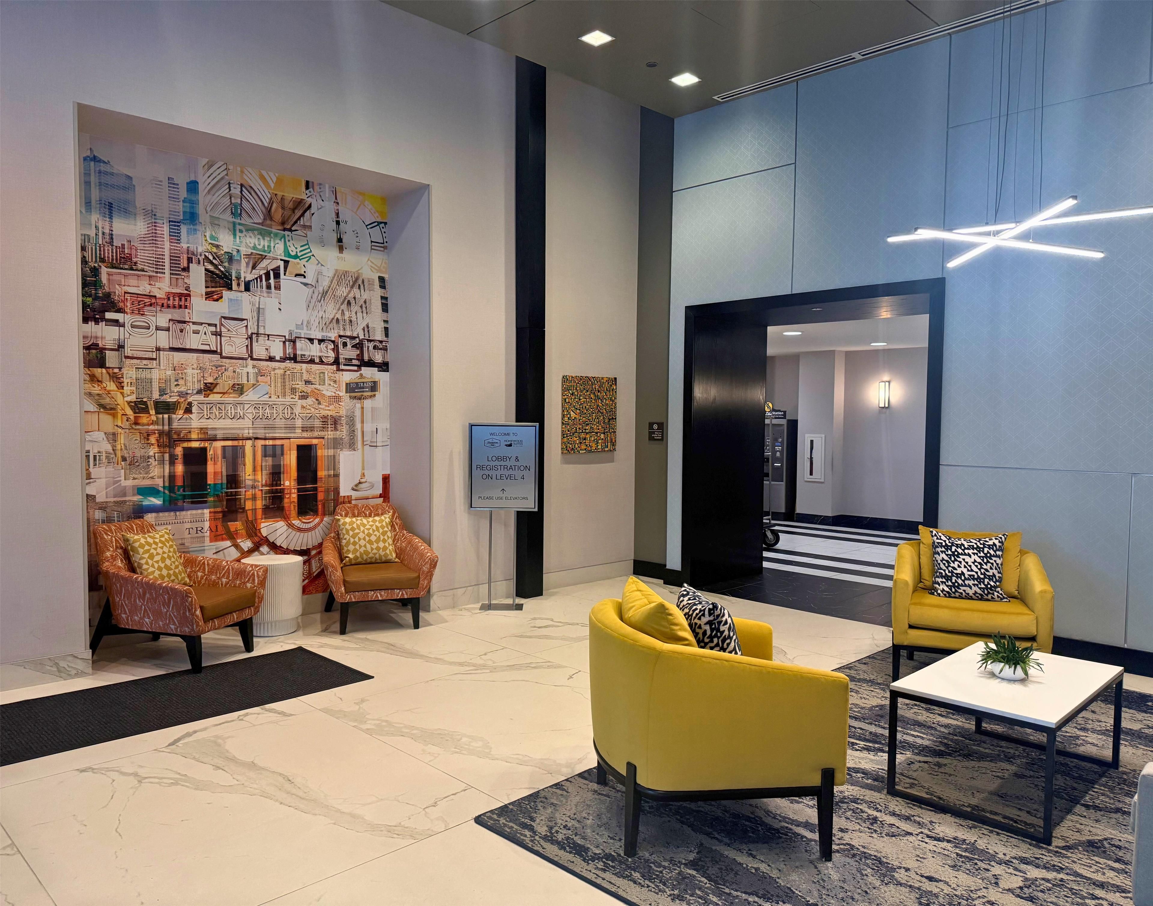 A lobby with a cityscape mural, two yellow armchairs, a coffee table, and a sign indicating registration on level 4.