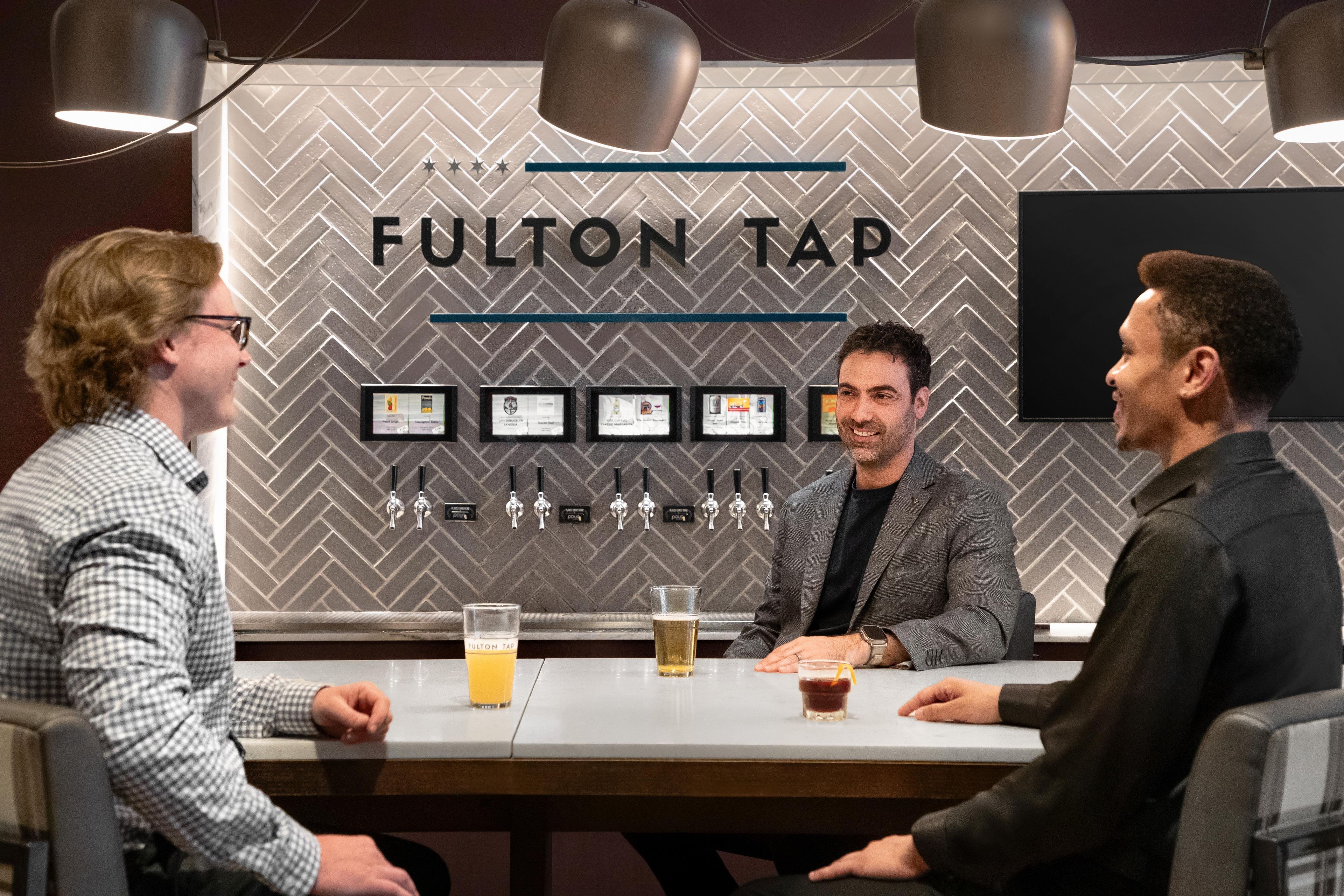 A bar setting with a sign reading 'FULTON TAP' and multiple beer taps.