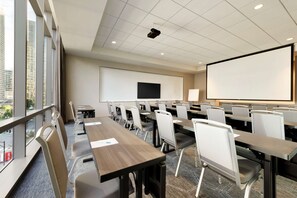 Un salón de conferencias con una pantalla grande, varias mesas y sillas.