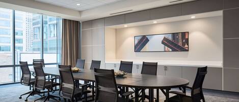 A conference room with a large table, chairs, a cityscape painting, and large windows.
