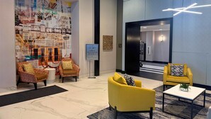 A lobby with a cityscape mural, two yellow armchairs, a coffee table, and a sign indicating registration on level 4. - Hampton Inn Chicago West Loop Fulton Market Area (Chicago)