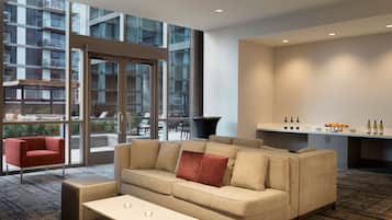 A modern hotel room with a sofa, a small table, and a view of the city through large windows.