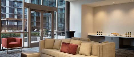 A modern hotel room with a sofa, a small table, and a view of the city through large windows.