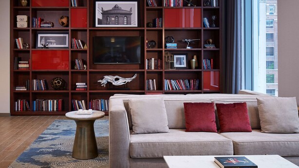 A living room with a sofa, coffee table, and a bookshelf filled with books and decorative items. - Hampton Inn Chicago West Loop Fulton Market Area (Chicago)