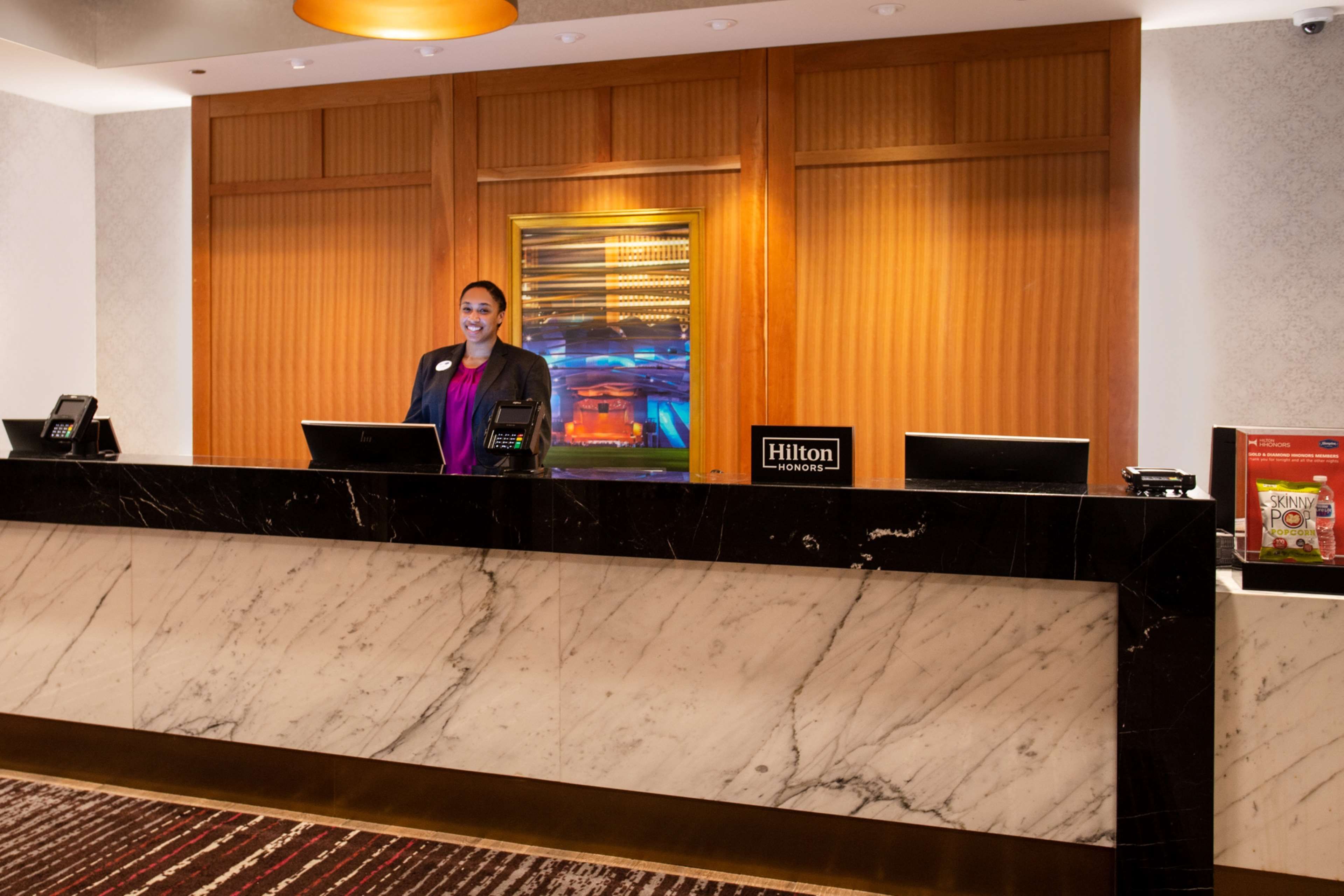 A hotel reception desk with a marble counter, a digital screen displaying the hotel's name, and a sign for Hilton Honors.