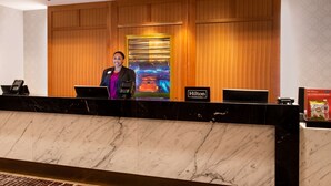 Mostrador de recepción de hotel con encimera de mármol, una pantalla digital que muestra el nombre del hotel y un cartel de Hilton Honors.