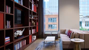 A modern living room with a large bookshelf, a sofa, a coffee table, and a view of the cityscape.