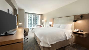 Hotelkamer met een bed, een bureau met televisie, een stoel, een nachtkastje met lamp en een raam met uitzicht op gebouwen.