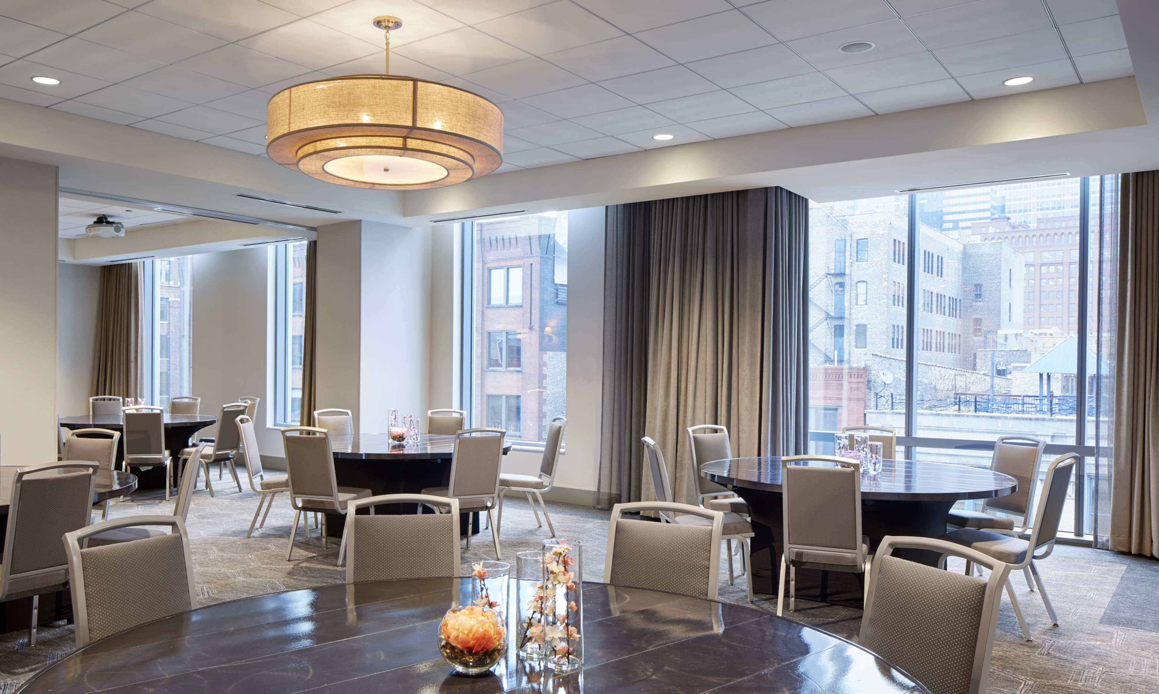 A modern conference room with round tables, comfortable chairs, and large windows offering city views.